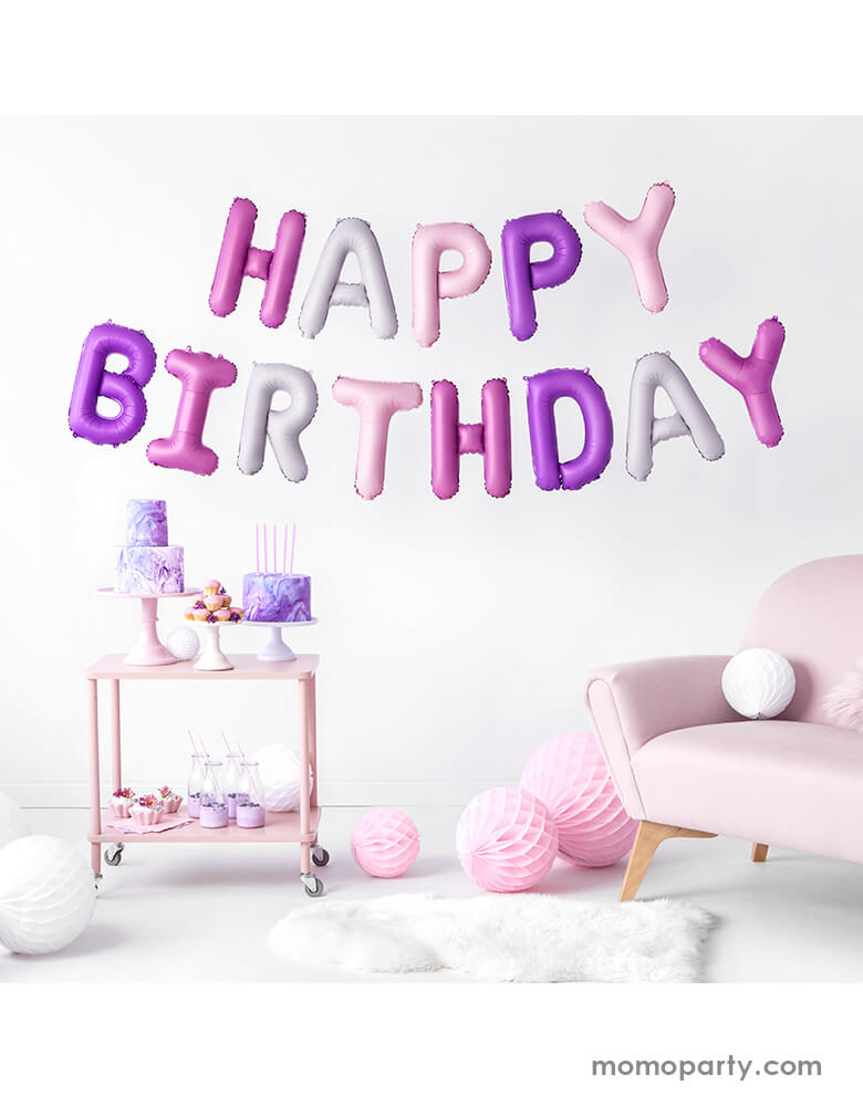 An at-home birthday party with pink couch and pink purple cakes and sweets with Party Deco's Pink Happy Birthday Foil Balloon Set in difference shade of pink hung on the wall for a girl's birthday