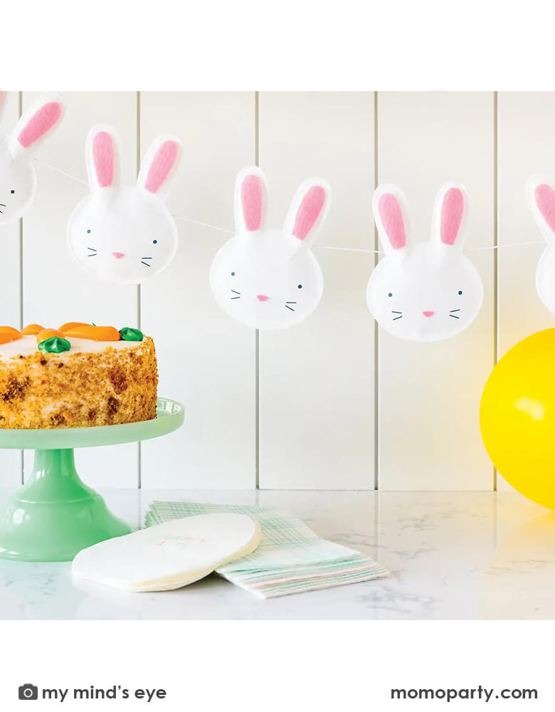 A kitchen counter decorated with Momo Party's 6 ft puffy felt bunny banner by My Mind's Eye, with a carrot cake and easter egg shaped napkins and blue gingham guest towels, it creates a simply yet unique look for an Easter celebration.