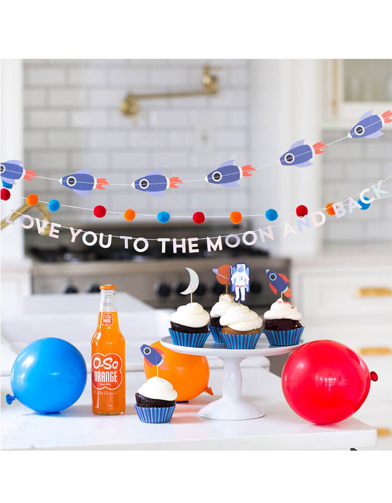 A space themed party table with My Mind's Eye Rocket Mini Banner Set hung above cupcakes and party balloons