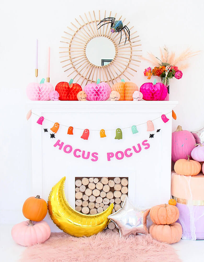 A pink boho Halloween mantel decoration idea featuring Kailo Chic's felt rainbow ghosts banner and Hocus Pocus felt banner. On the mantel there were pink and blush pumpkin honeycomb decorations, perfect for a not-so-scary kid's friendly Halloween celebration.
