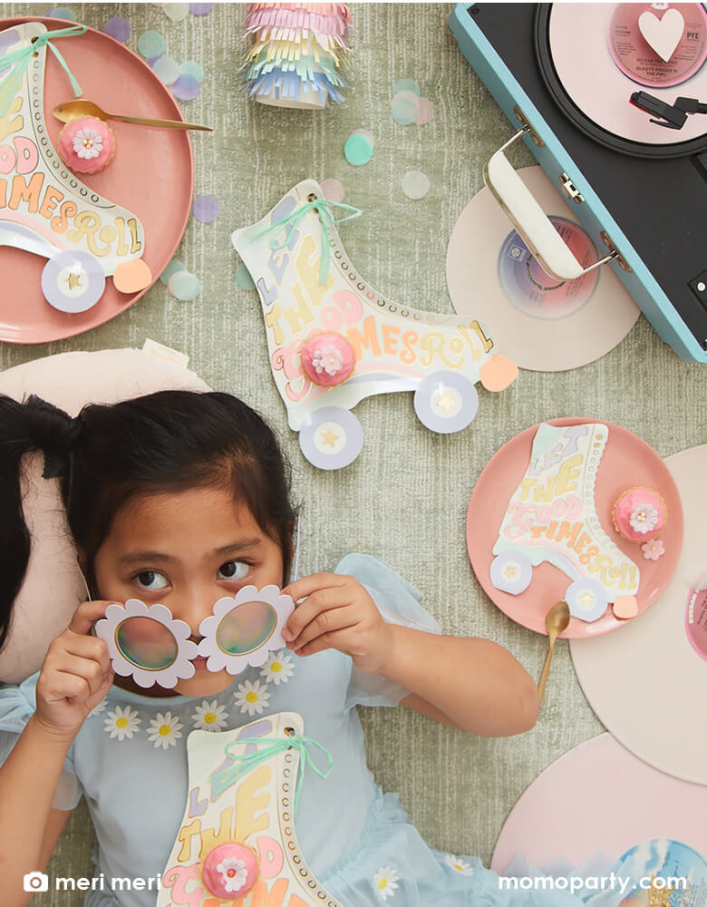 A little girl wearing a white daisy shaped sunglasses lying on the ground with some retro roller skates and a vintage record player with Momo Party's Roller Skate shaped Party tablewares including napkins, plates and party cups around. With pastel confetti spread across, this makes a festive scene for a retro inspired celebration for kids!