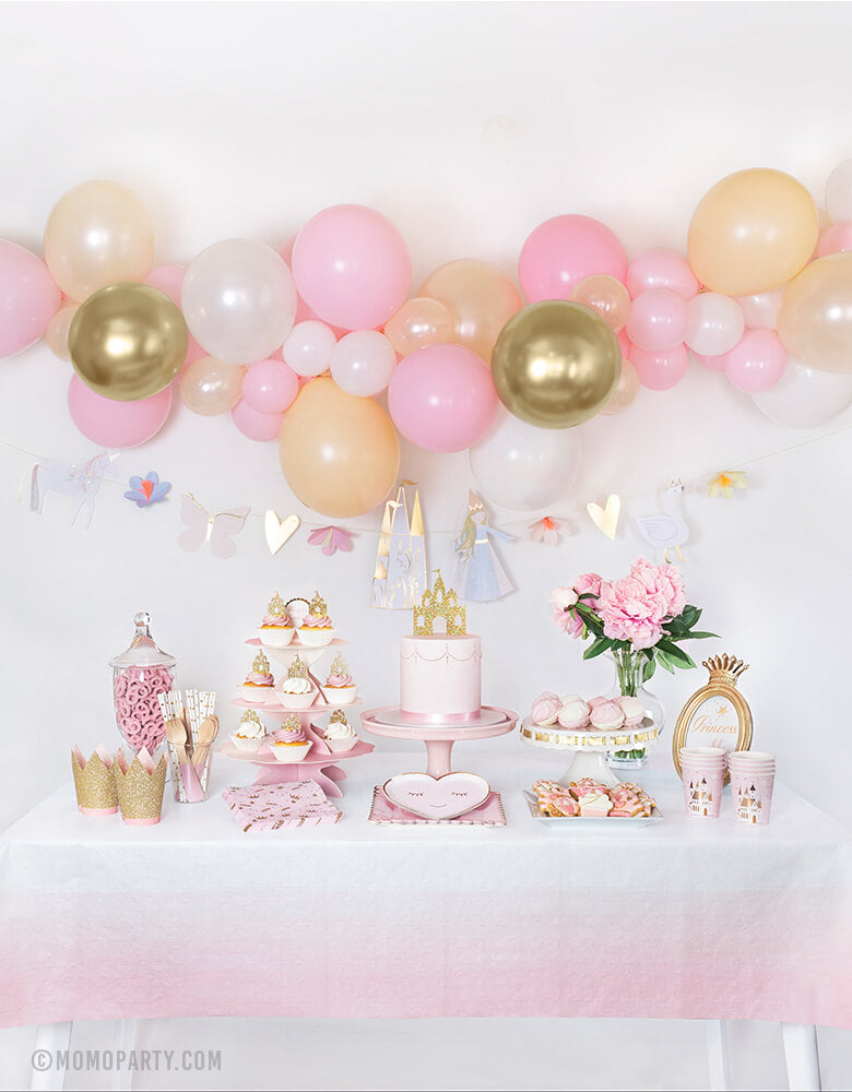 Royal Princess party dessert table with backdrop decoration idea, feathered a Diy balloon garland made with Qualatex latex balloons, Meri Meri Magical Princess Garland. On the dessert table, a Pastel pink cake with Princess Castle Cake Topper on top, Meri Meri Blushing Heart Plates layered with Blush Large Plates in the middle, Day Dream Society Sweet Princess Cups and Napkins on the side, Cupcakes with Princess Castle Cupcake Toppers on pink cake stand. for Royal princess birthday party celebration