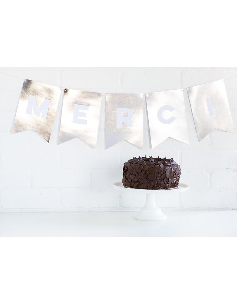 My Minds Eye Paperlove Silver Letter Banner with Merci spelled out on the wall with a chocolate cake on the table