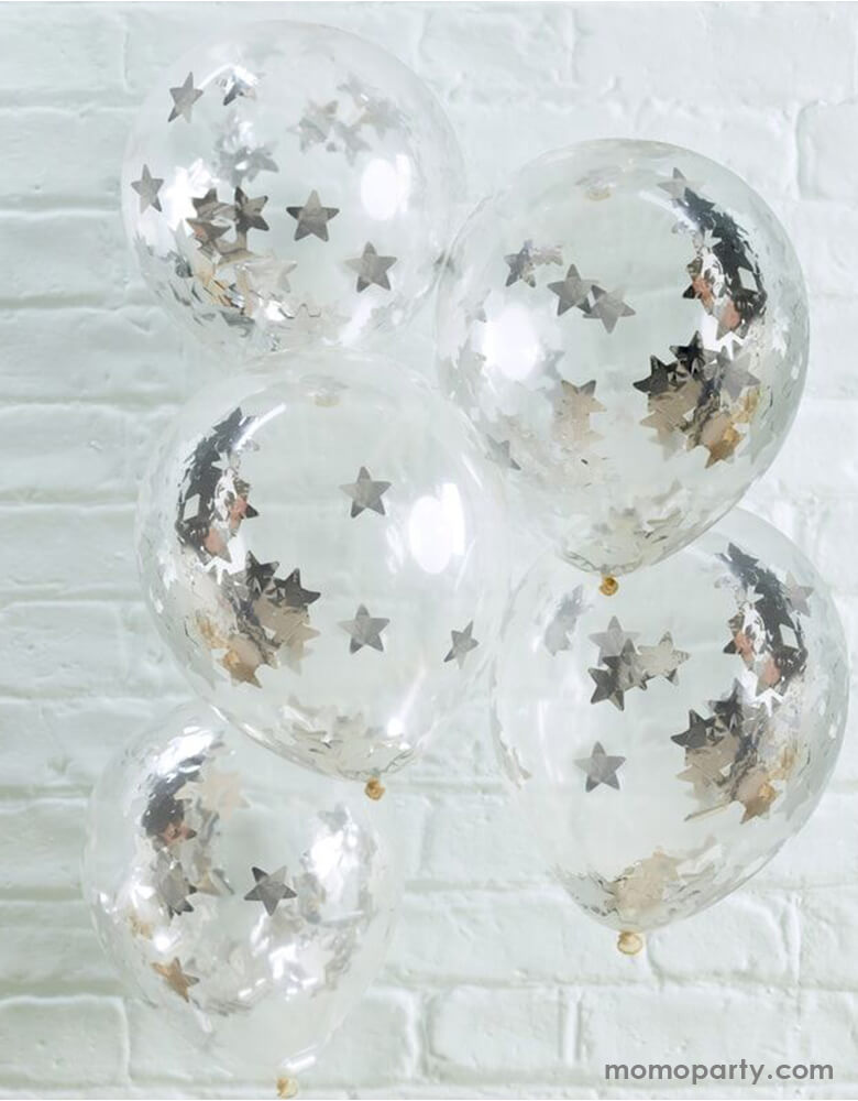 A bunch of Ginger Ray 12" clear confetti balloons pre-filled with silver star shaped confetti in front of a white brick wall makes a perfect decoration for a space or superhero themed kid's birthday party