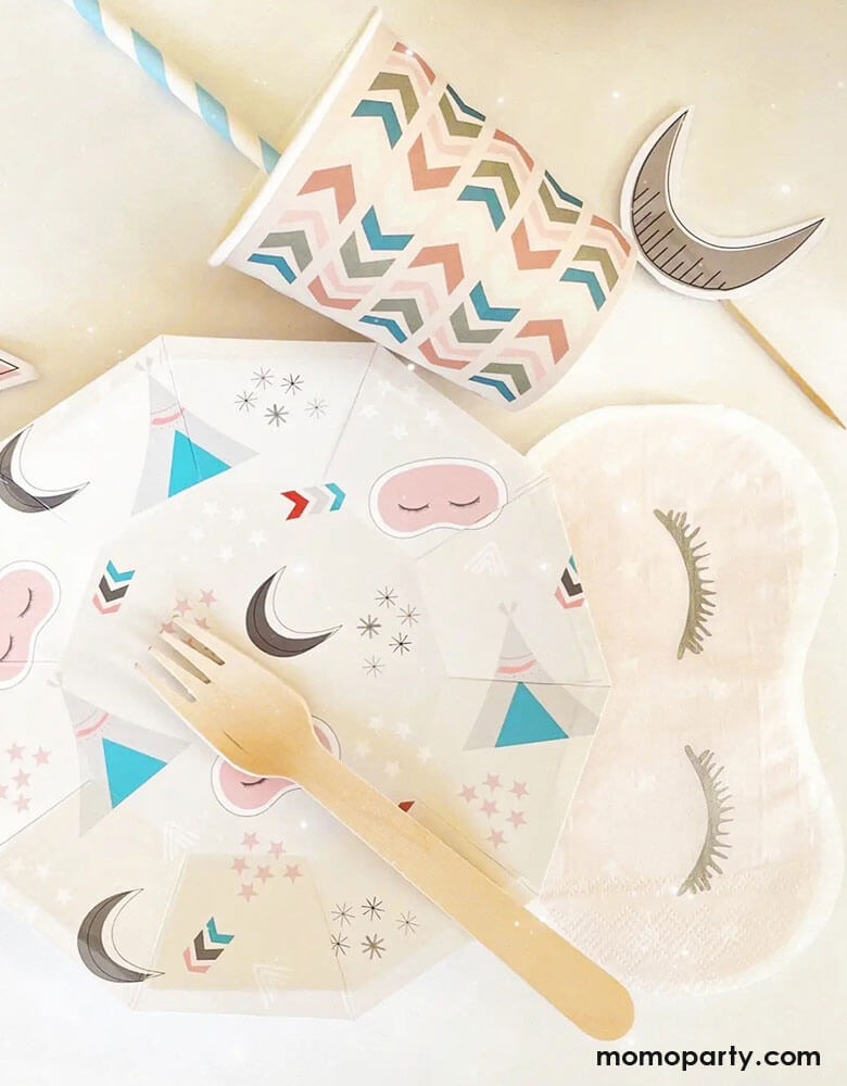 A tablescape of girls sleepover party featuring Momo Party's sleepover napkins in the shape of sleeping masks by Pooka Party, along with coordinated plates featuring sleepover themed illustrations like sleeping tents, sleeping masks, moons and stars, plus light pink party cups with chevron design, and cupcake topers with moon design, perfect for girl's slumber party.