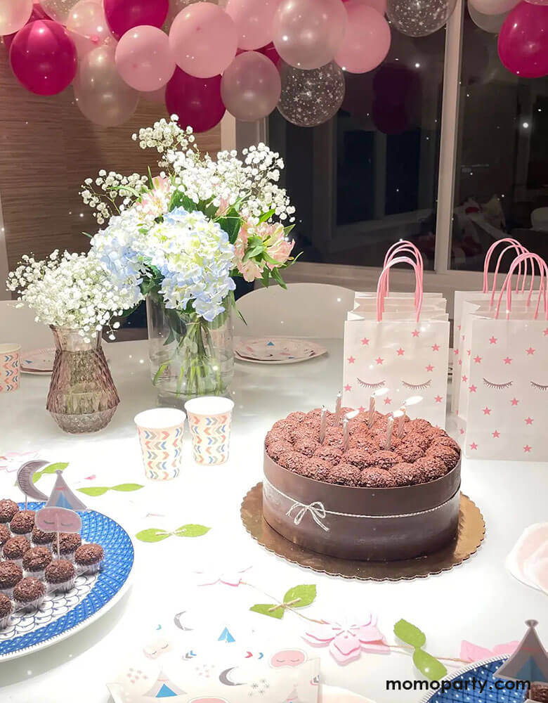 A sleepover slumber party featuring a chocolate cake, some cupcakes and Momo Party's 8.2 x 5.9 x 3.15 inches sleepover party bags with sleepy eyes and pink star designs by Pooka Party, comes in set of 8. In the background the room was decorated with pink, rose, and rose gold balloon garland with beautiful flower bouquet, makes a great inspiration for girls birthday party ideas.