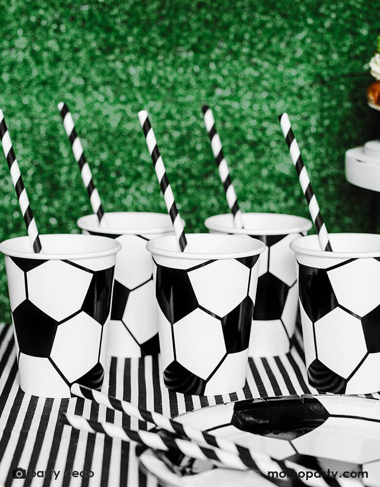 A table filled with soccer themed tableware including  Momo Party's 6.8 oz Soccer ball party cups by Party Deco in classic black and white color, perfect for a kid's soccer themed birthday party or a World Cup soccer watching party!