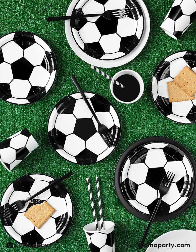 A table with filled with soccer themed tableware including  Momo Party's 6.8 oz Soccer ball party cups by Party Deco in classic black and white color, perfect for a kid's soccer themed birthday party or a World Cup soccer watching party!