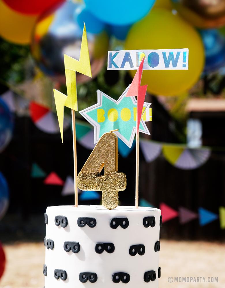 Super Hero themed Birthday Cake design with MeriMeri Zap! Superhero Cake Toppers of Bright Cosmic sign, lighting bolts and superhero-themed headlines "Boom" 'Kapow!" and Talking Tables We Heart Birthday Glitter Candle - Goldgold glitter dipped number 4 candle for 4 years old boy's modern superhero birthday party