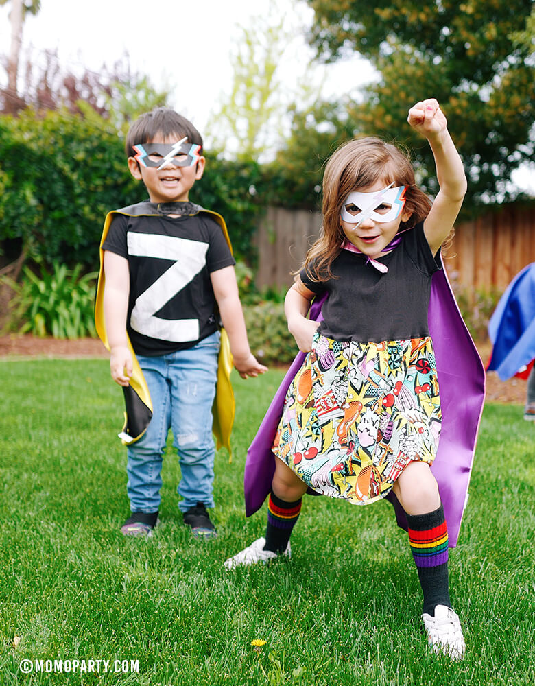 Boy and girl wearing Meri Meri Super Hero Masks and capes in a outdoor superhero birthday party. girl power birthday party. girl superhero party