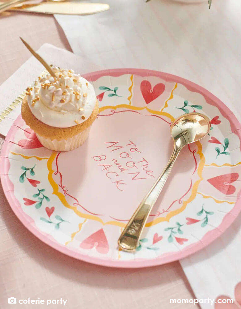 A beautiful love themed party table featuring Momo Party's 9 oz pale pink pinstripe party cups by Coterie Party and 9" All You Need is Love Large Plates with a message of "To the moon and back" on the plate. With a table set with pastel pink themed tableware with heart shaped elements, it's a perfect inspiration for a Valentine's Day celebration.