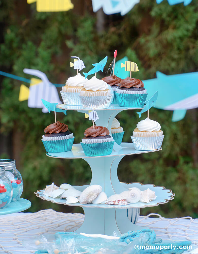 Under the sea party table idea. cupcake decorated with Under The Sea Cupcake Kit, on a 3 tier light blue cake stand. the bottom tire decorated with sea shells. These beautifully crafted toppers of sea friends like shark, fish, jellyfish and coral, takes on an underwater adventure sea themed party celebration! Party set up, partywares and Photo by Party Boutique Online at momoparty.com