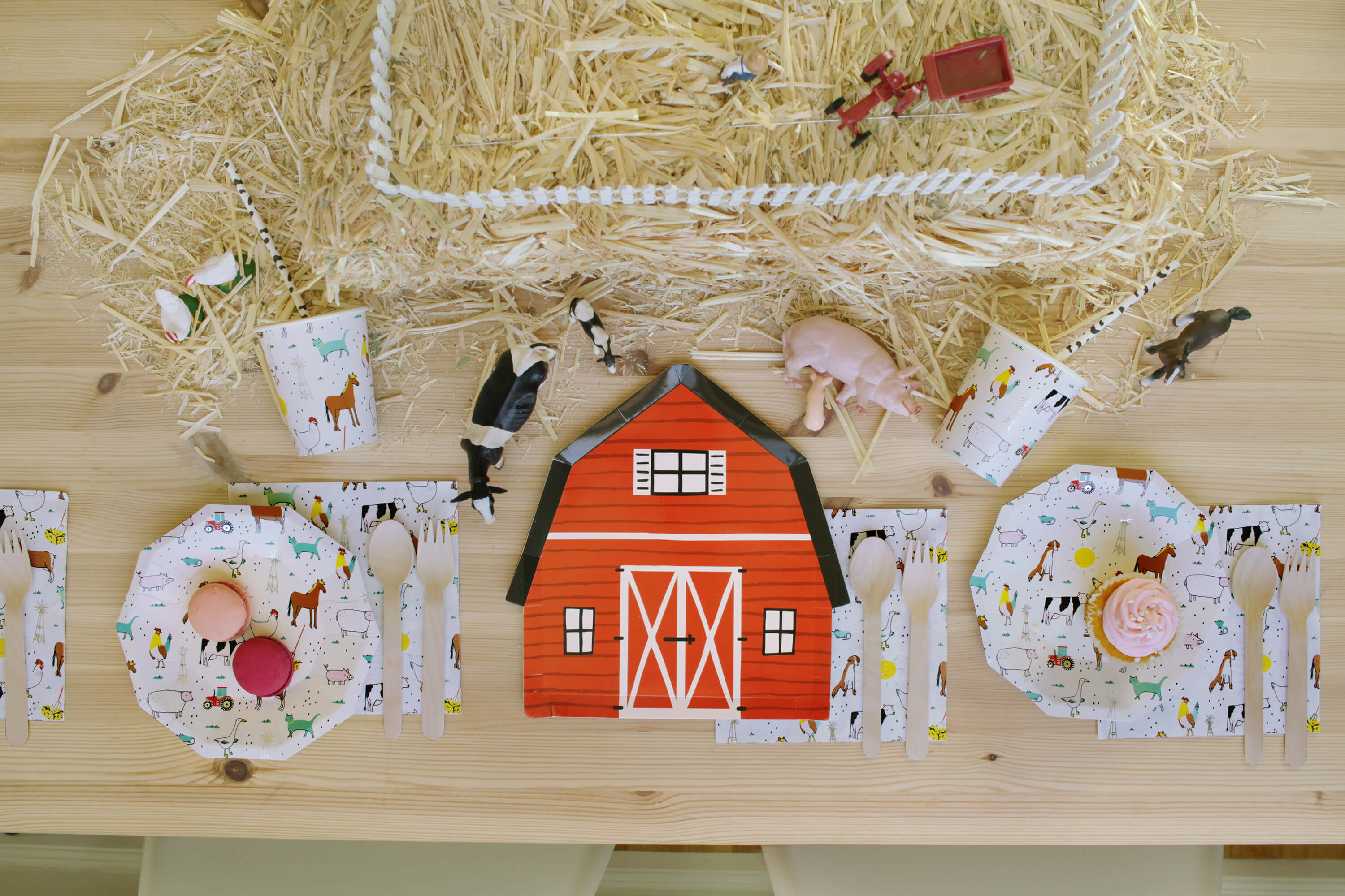 Barnyard Farm Themed Party for Kids, with a barnyard plates, farm animal plates, napkins, cups and sweets on top of a wooden textured dining table, table Styled by momo party