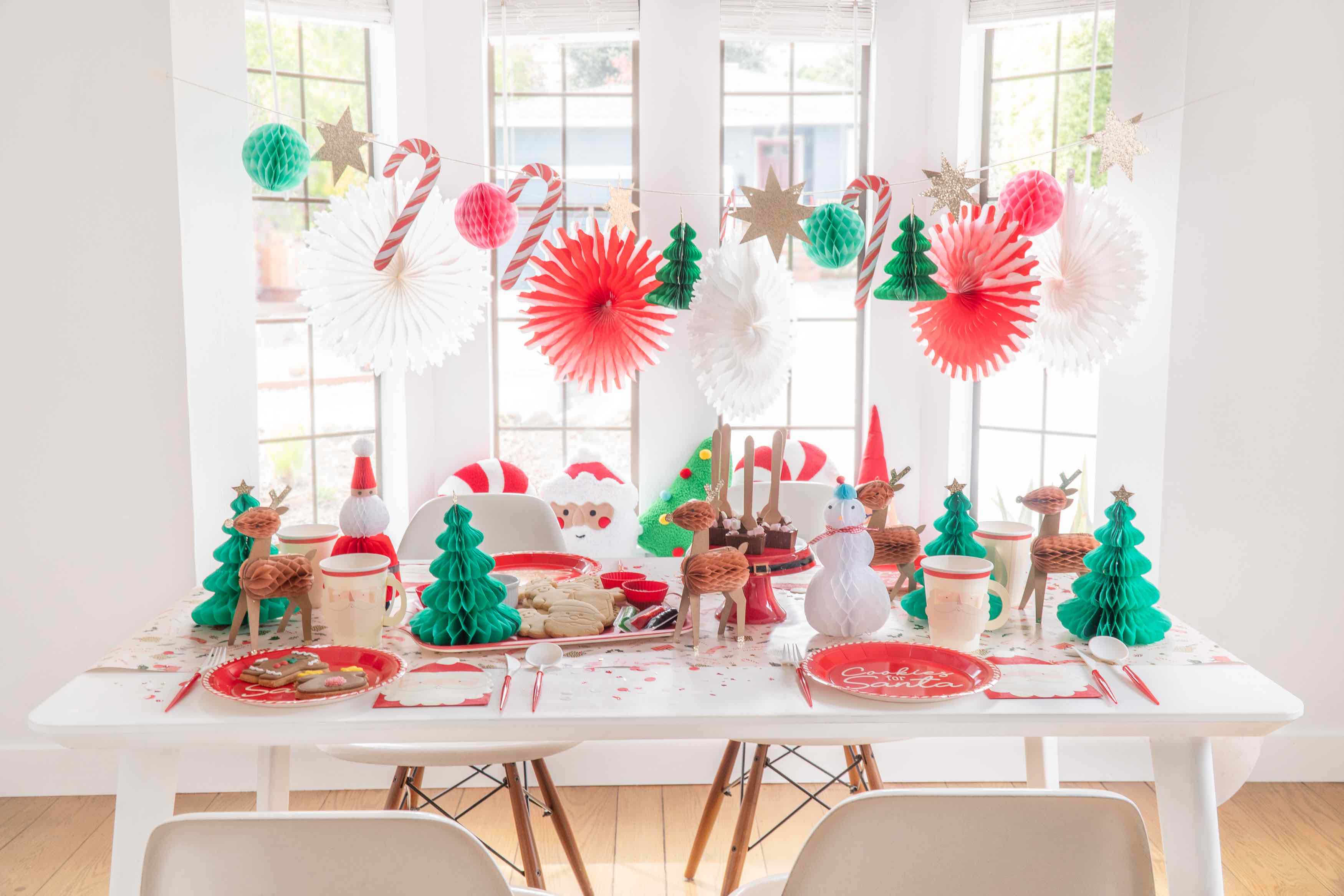 How to host a Christmas cookie decorating party for kids by Momo Party featuring festive Christmas honeycomb garland with candy canes, peppermints, Christmas trees hung next to the windows. On the table are Christmas character honeycombs with Santa.