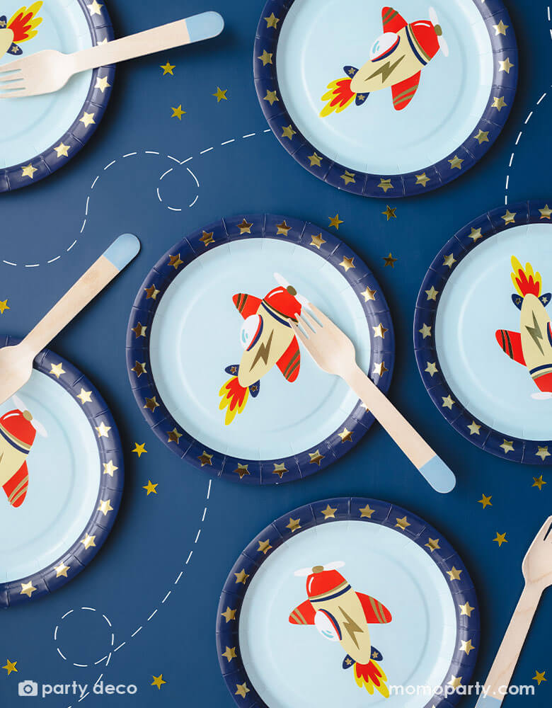 A navy blue table featuring 6 of Momo Party's 7" Airplane Round Paper Plates and blue dipped wooden forks by Party Deco. Featuring gold foil stars around the edge and a vintage cream and red colored airplane design on a blue sky light blue background, this set of 6 round plates are perfect for your kid's plane or aviation themed celebration.