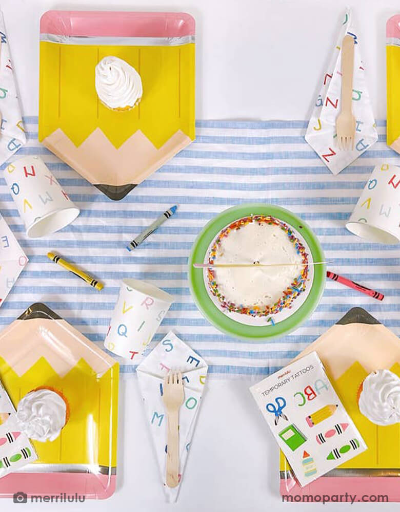 A school themed party table filled with Momo Party's school themed party supplies including a pencil shaped plate, ABC alphabet patterned napkins, plates and cups. Next to the tableware there's a cake topped with a pencil shaped cake topper with "Hello 2nd Grade". On the pencil plate, there's a tattoo sheet featuring colorful school themed designs including crayon, glue bottle, notebook and more. All this makes a great inspo for a back to school party or first day of school celebration.