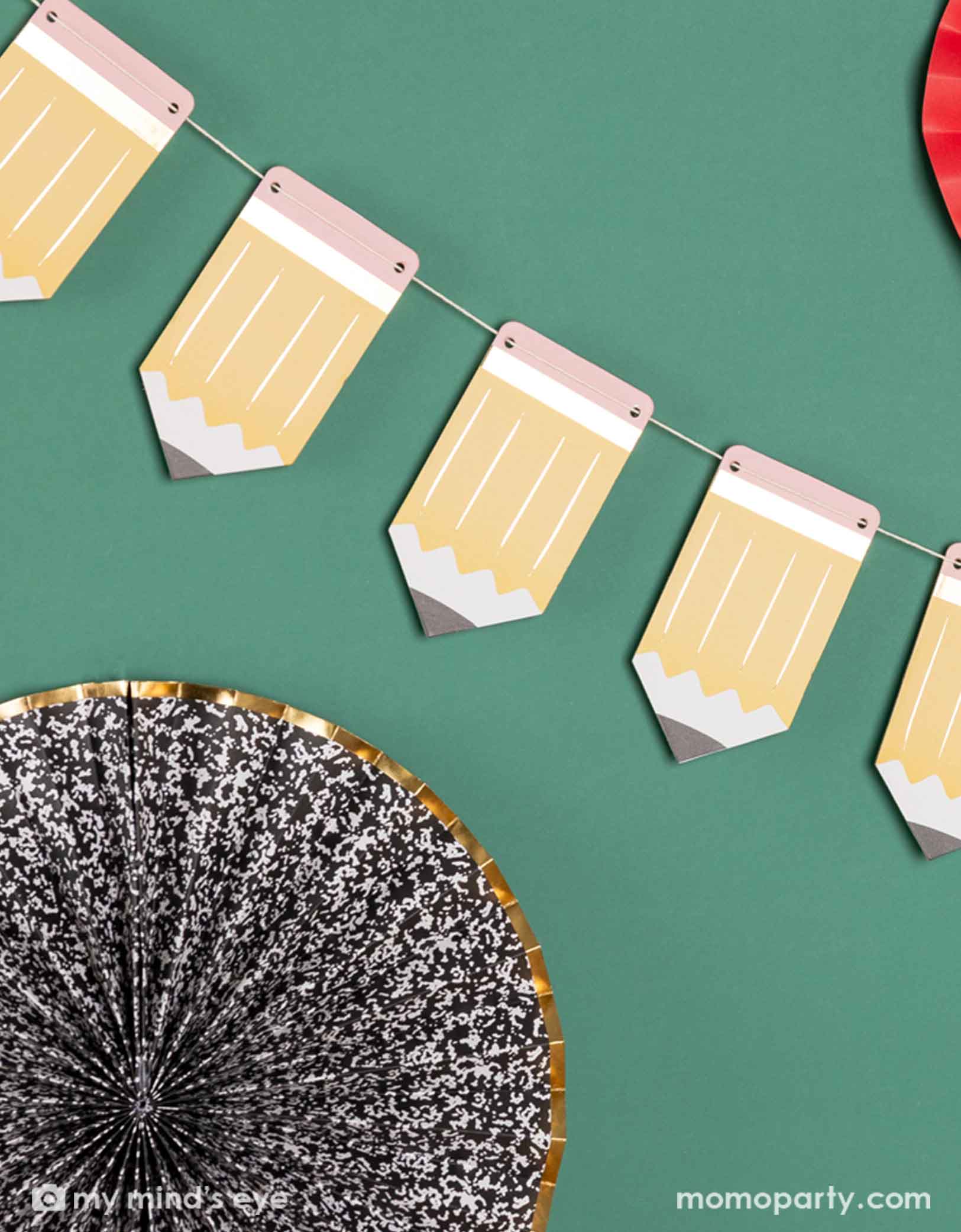 A green chalkboard decorated with the 5' pencil shaped party banner and apple, notebook shaped paper fans from Momo Party. A modern and easy decoration to celebration kid's back to school or first day of school special day.