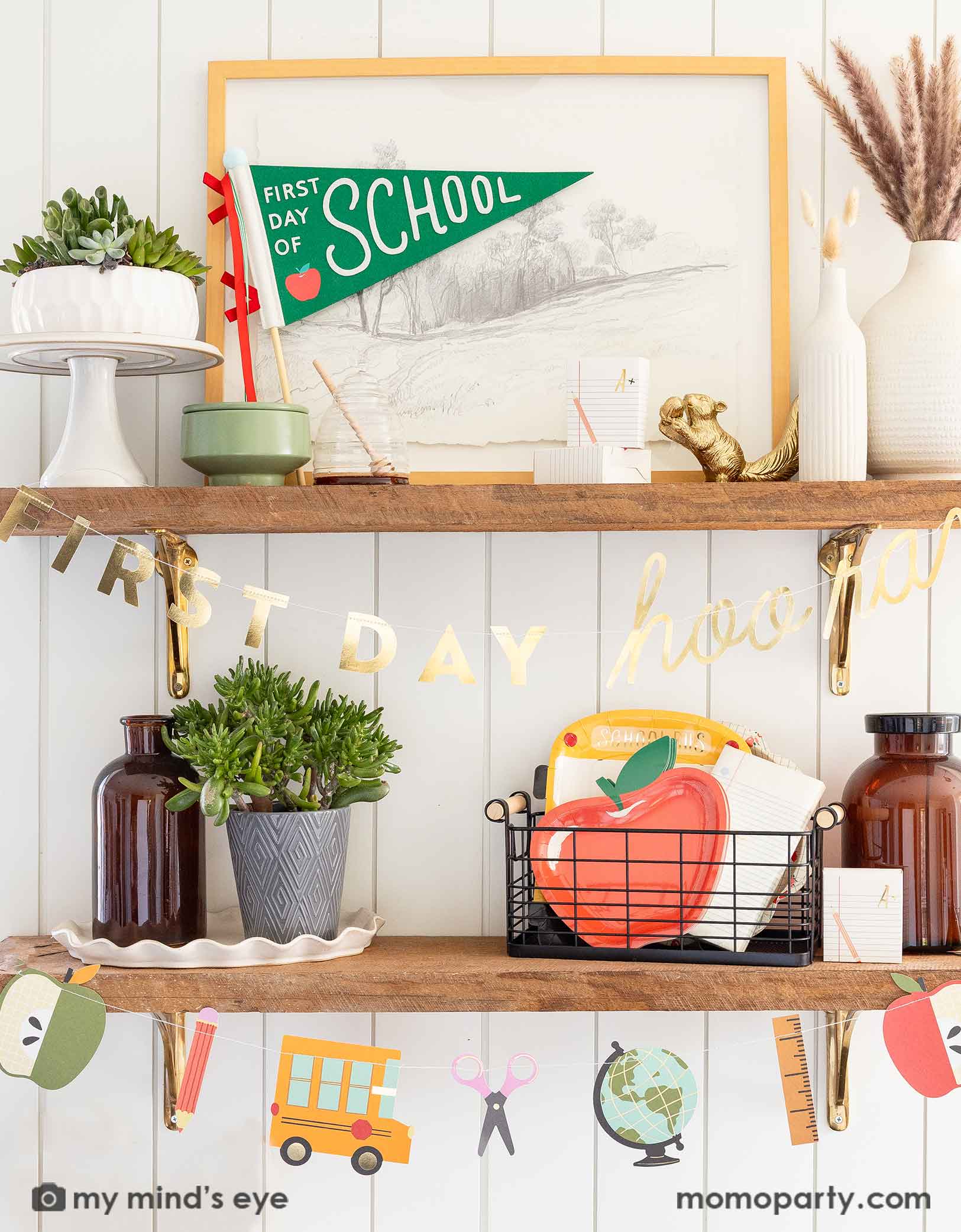 A shelf decorated with various school themed party supplies and decorations from Momo Party including the 'First Day of School' apple party pennant, the first day of school party garland featuring school supply shaped pennants like scissors, rulers, apples, globes and school buses.  On the shelf there is a basket filled with school themed party tablewares including apple shaped plates, school bus shaped plates, notebook napkins. A modern home decoration idea to celebrate kid's first day of school.