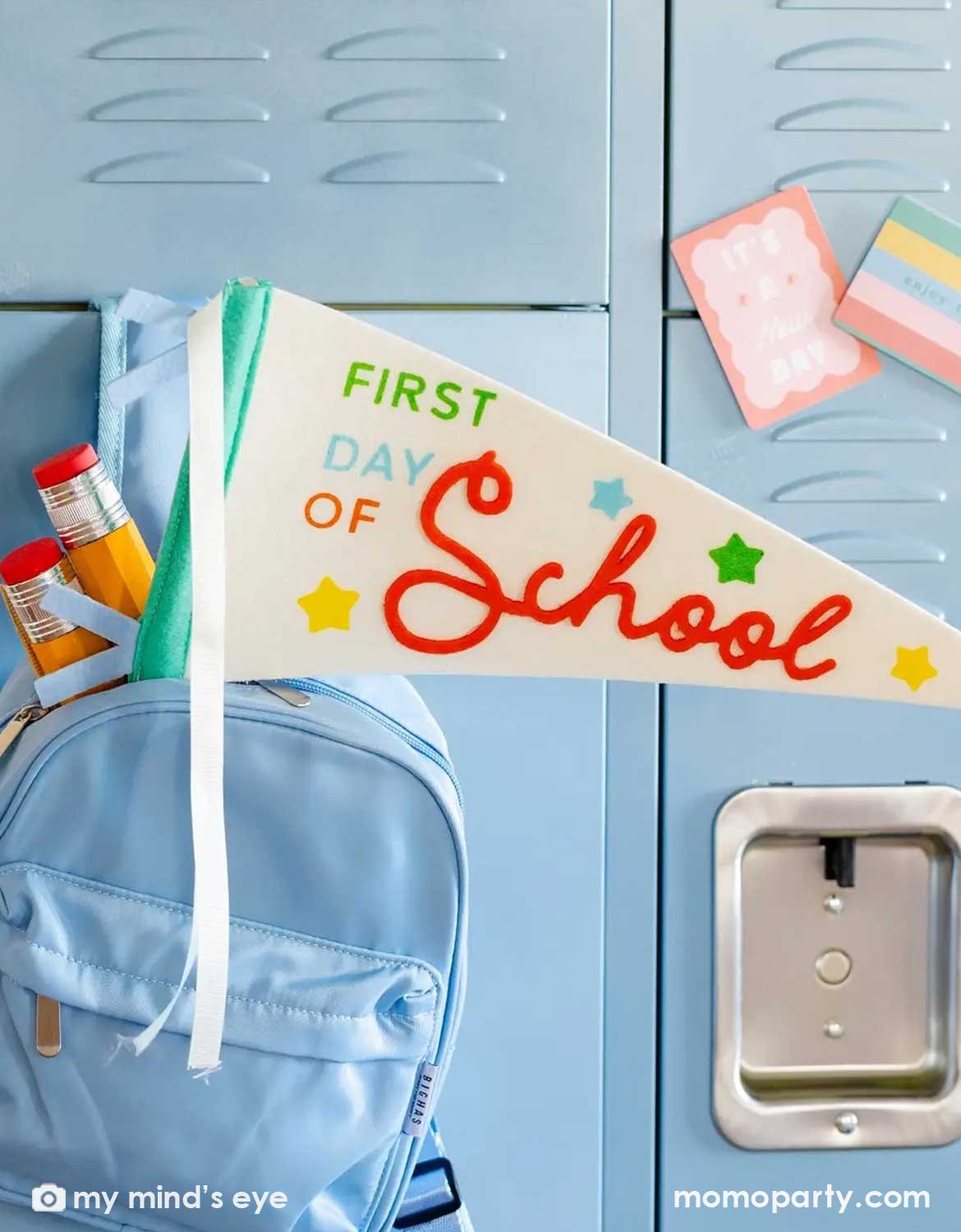 Momo Party's colorful 'First Day of School' party pennant on a blue backpack with stationery on a blue locker background in a classroom setting.