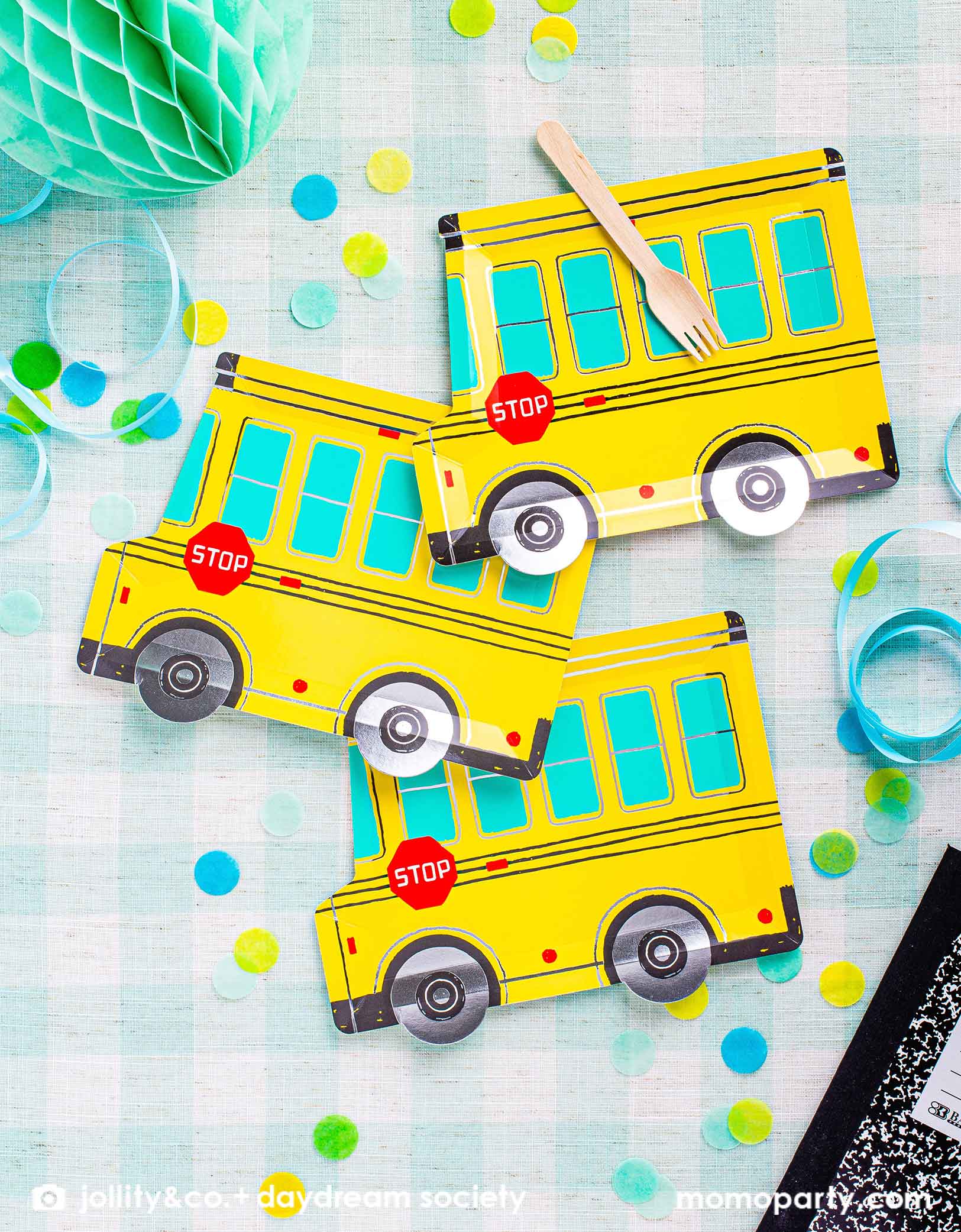 A festive back to school party tablescape featuring Momo Party's colorful school themed tableware including Daydream Society's school bus shaped plates and some school notebooks on a mint gingham checkered tablecloth. With a mint honeycomb decoration and some bright colored confetti, this gives a great visual inspiration for a kid's back to school party or a first day of school celebration.