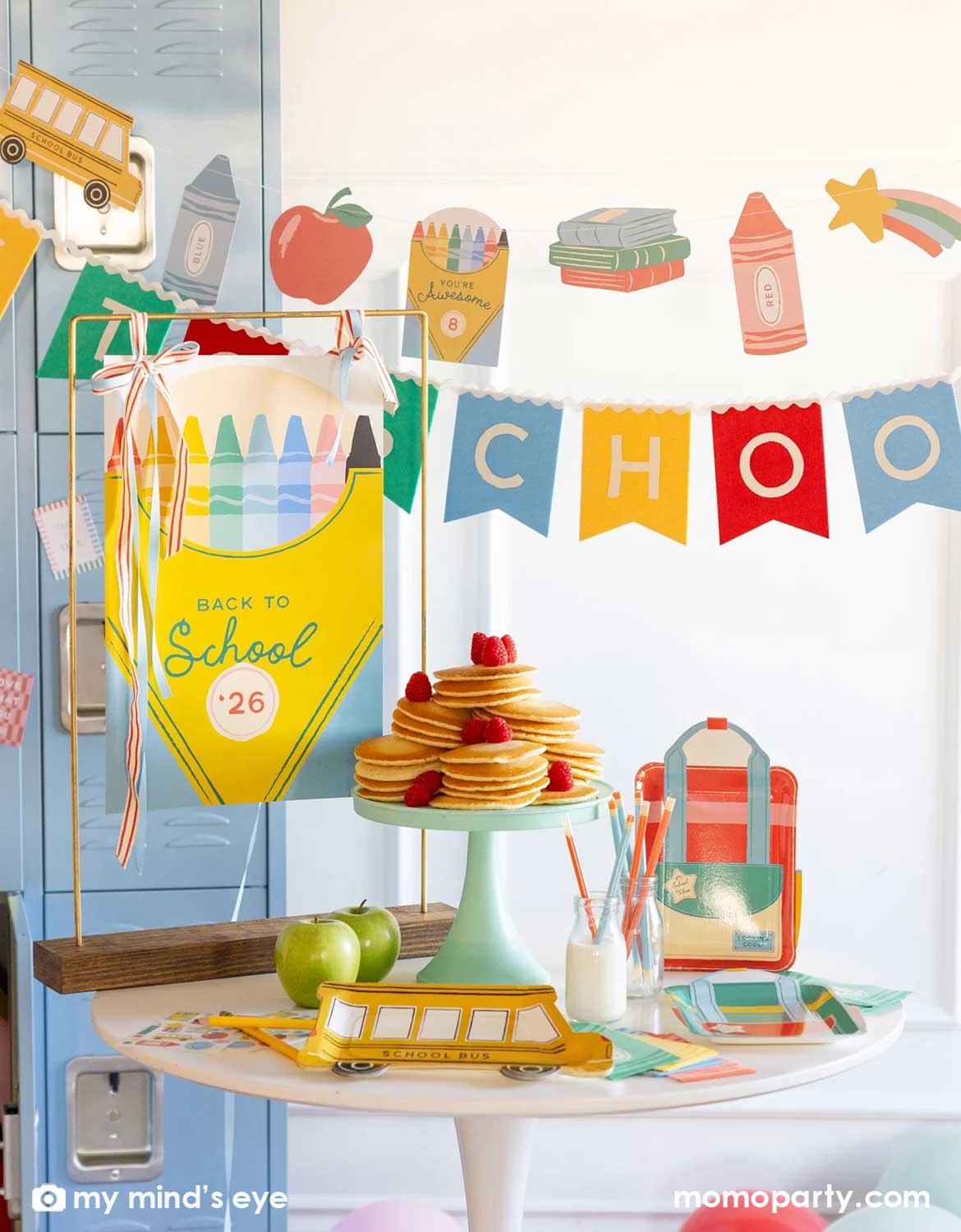 A close-up shot of a back to school classroom set up featuring various school themed party supplies and decors from Momo Party including school themed plates, treat boxes, party pennant, back to school felt garland along with school icons party banner hung above the light blue locker selves. A party table with pancakes on a cake stand next to some colorful backpack shaped treat bags.