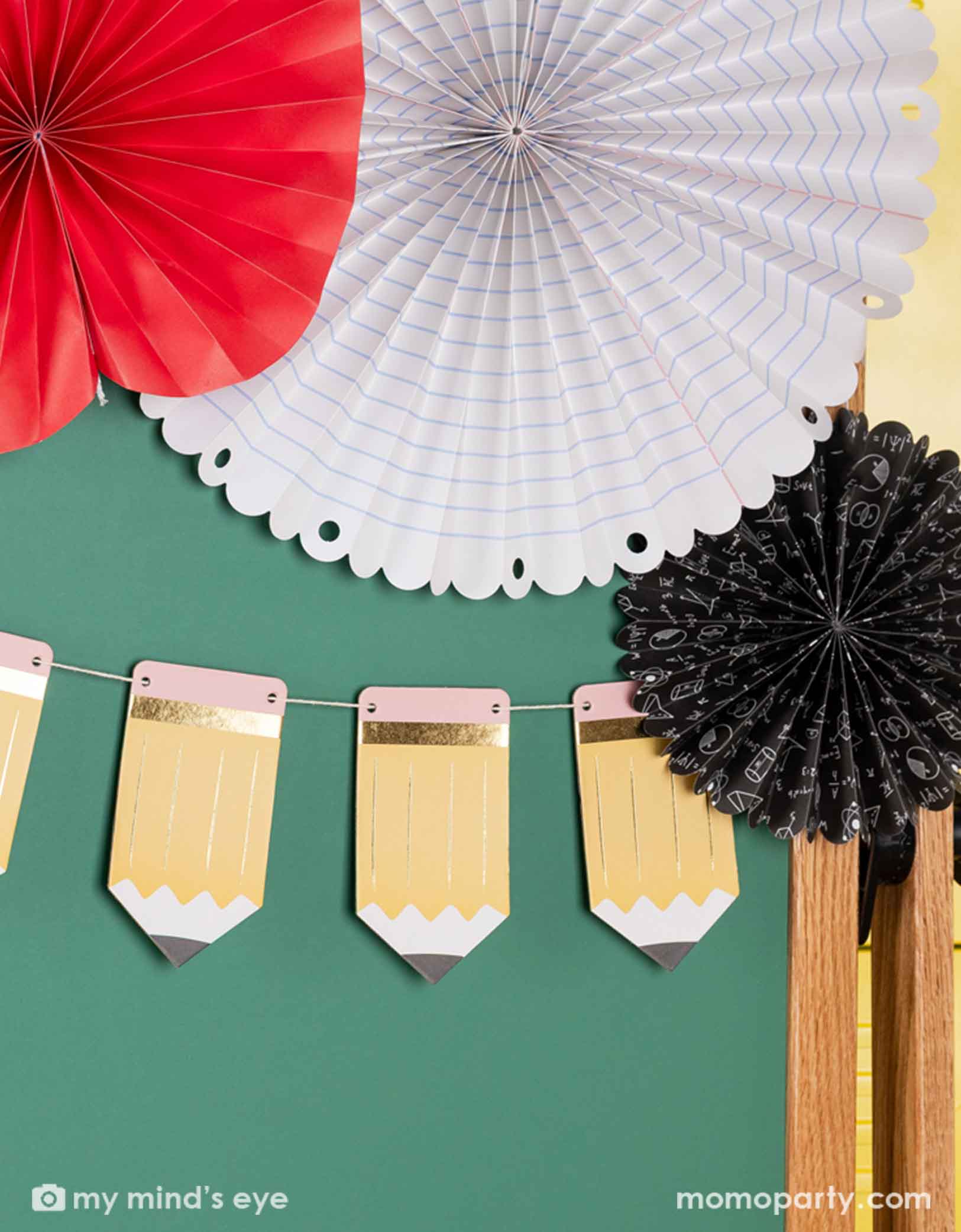 A green chalkboard decorated with the 5' pencil shaped party banner and apple, notebook shaped paper fans from Momo Party. A modern and easy decoration to celebration kid's back to school or first day of school special day.