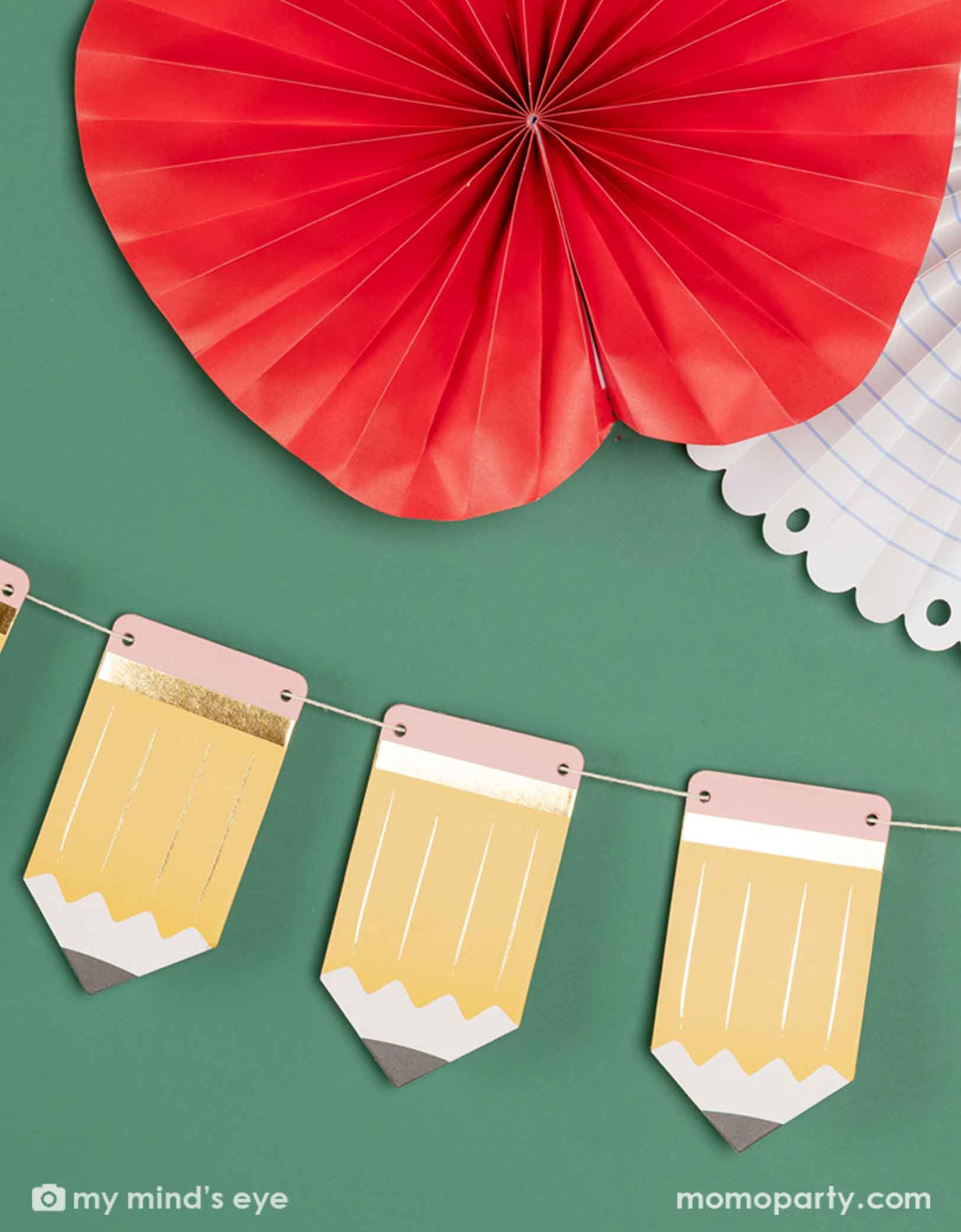 A green chalkboard decorated with the 5' pencil shaped party banner and apple, notebook shaped paper fans from Momo Party. A modern and easy decoration to celebration kid's back to school or first day of school special day.