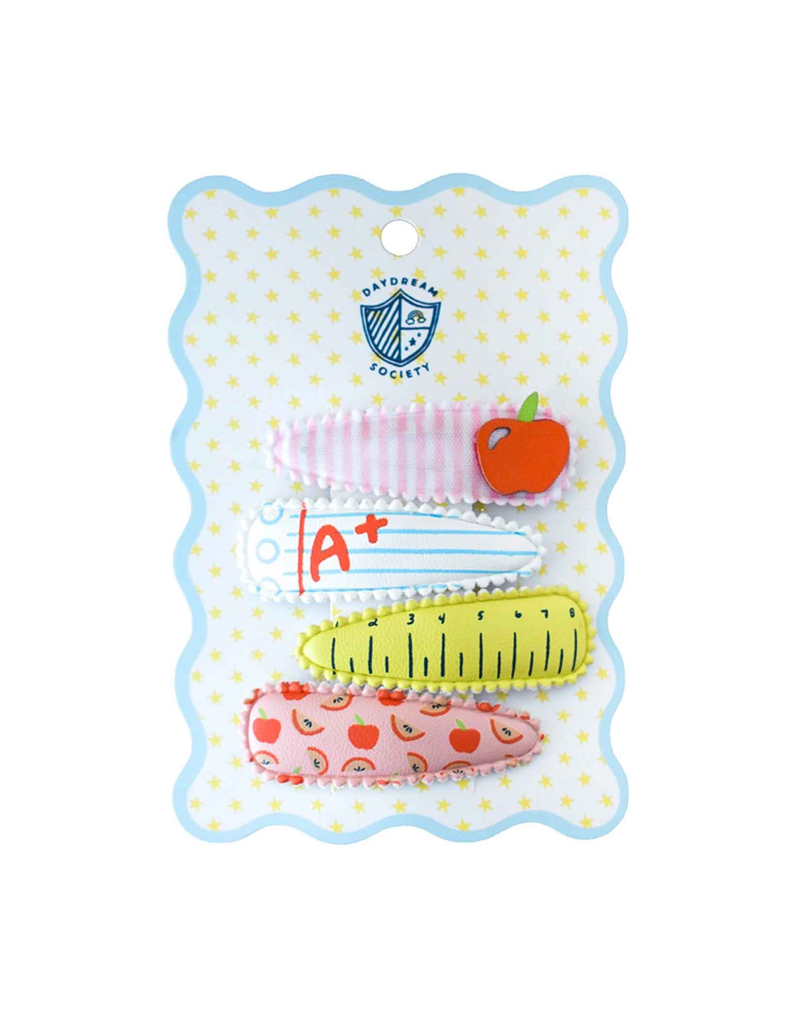 Momo Party's Smarty Pants ABC Hair Clip Set by Daydream Society. Four hair clips, one with a notebook design with A+ on it, one with an apple design on a red and white stripe background, one with apple and rainbow patterned design, and one with a ruler design, on a polka dot card with wavy edge. These hair clips are perfect for back to school picture day, first day of school, and every school day in between.