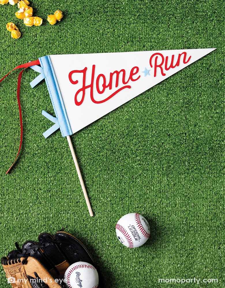 Momo Party's baseball HOME RUN felt party pennant by My Mind's Eye on a faux grass table with baseball mitt and baseballs around, with some popcorn, a perfect inspo for kid's baseball themed party celebration!