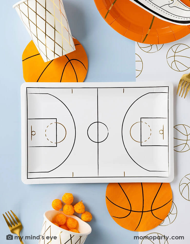 A basketball themed party table features Momo Party's basketball tableware by My Mind's Eye including basketball shaped plates, napkins, basketball court shaped large plates, basketball net gold foil party cups and paper basketball table runner - a perfect table setting inspo for kid's basketball themed birthday parties or a fun NBA viewing party!