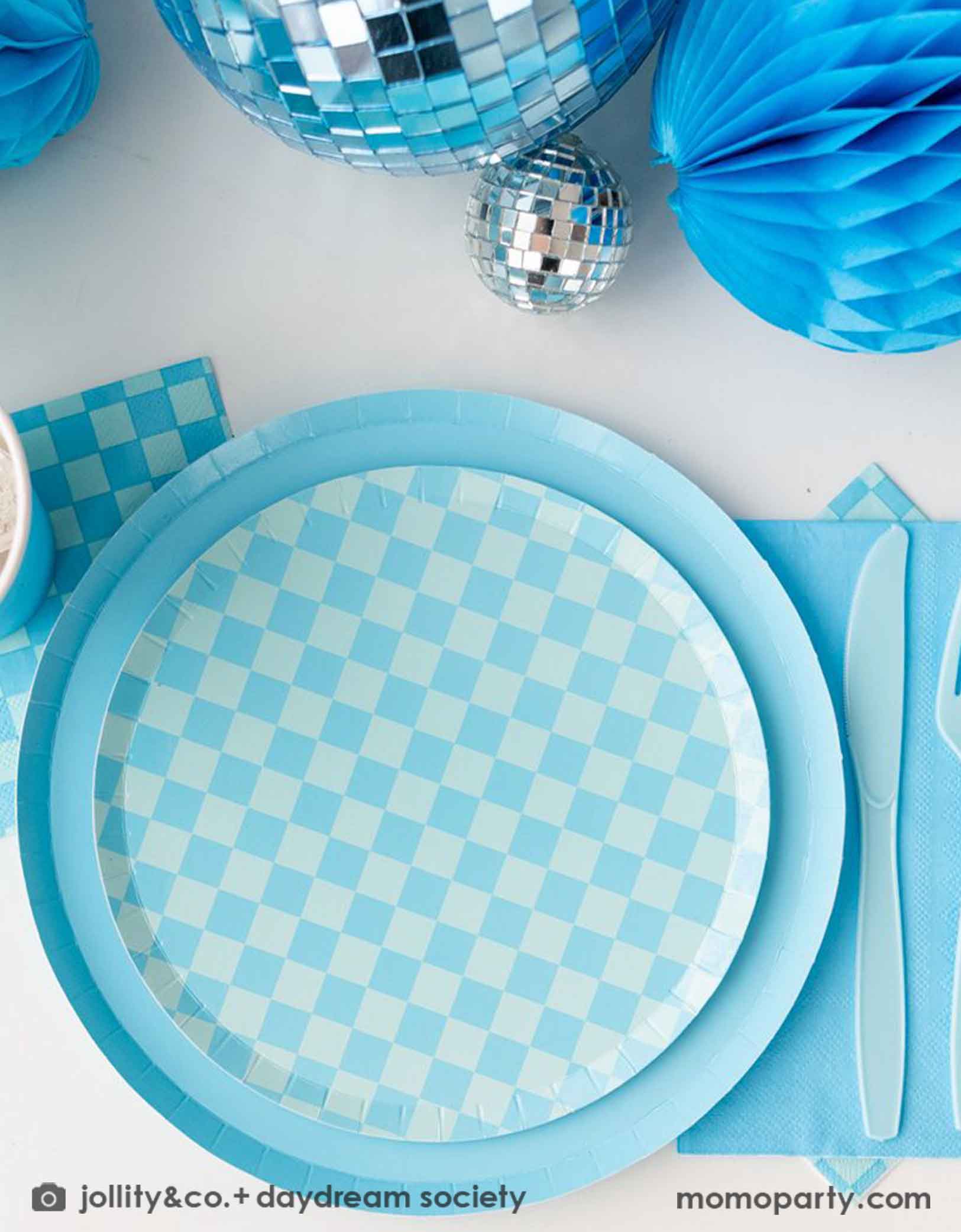 A blue themed party table features Momo Party's Check it! Blue and Blue Checkered Tableware Collection by Jollity & Co. including 10" blue dinner plates, 8" blue checkered dessert plates, 6.5" large napkins, blue plastic utensils and solid blue party cups, with blue honeycomb and disco ball decorations as the centerpiece for the party table.