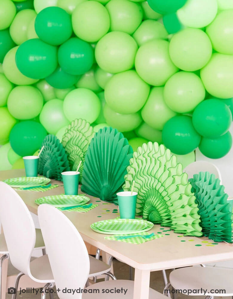 A green themed party set up featuring a giant green balloon wall in the backdrop. On the table features Momo Party's Check it! Lime Green Checkered Tableware Collection by Jollity & Co. including 10" dinner plates, 8" dessert plates, 6.5" large napkins and solid green party cups, with green paper fans as the centerpiece.