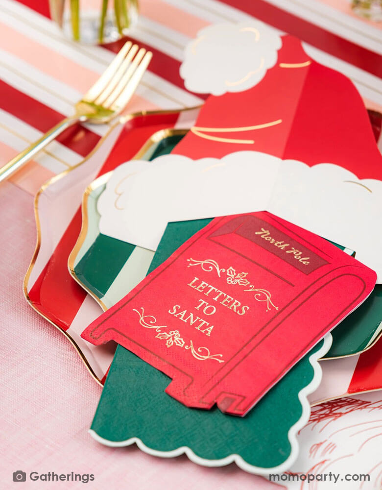 A festive Christmas party tablescape featuring Momo Party's Holiday red striped dinner plates and green side plates, along with a Santa hat shaped place card and a letter to Santa mail box shaped napkin, on a red and pink striped table runner. This makes a jolly table setting for this Holiday season.