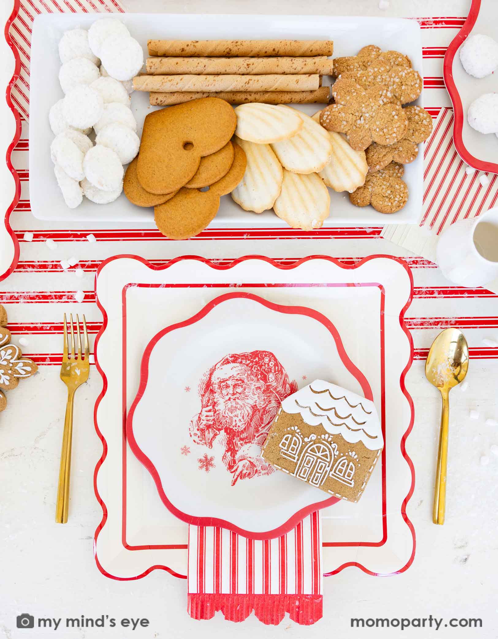 Christmas-themed table place setting with Holiday cookies, crackers, and decorative plates featuring a Santa Claus design, along with red striped scalloped dinner napkins and paper table runner from Momo Party.