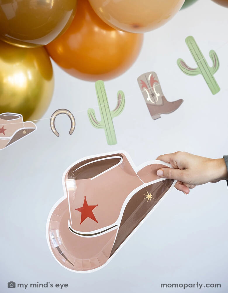 A cowboy Western themed party featuring Momo Party's cowboy themed party supplies including the Western themed party banner and cowboy hat shaped plate under some brown and gold colored balloon garland - a perfect decoration for a fun Western celebration or kid's First Rodeo cowboy themed first birthday.
