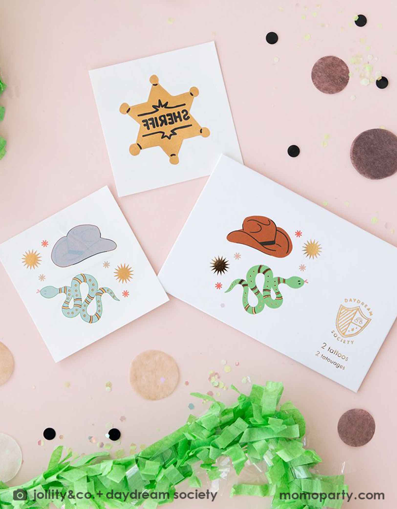 An overshot of Momo Party's Yeehaw Cowboy Temporary Tattoos by Daydream Society.  These temporary tattoos feature designs of a cowboy hat, snake, and sheriff badge in shiny gold foil. Around the temporary tattoo sheets there are some brown round confetti and some green streamers. They make perfect party favors for kid's Western or cowboy themed birthday celebration!