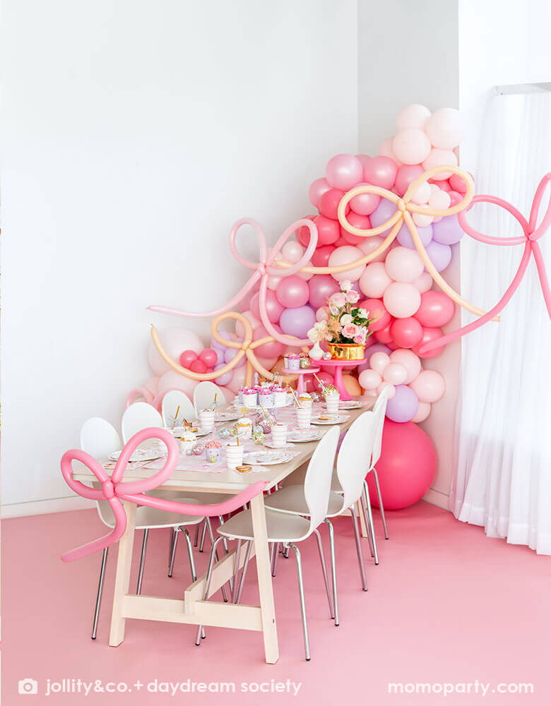 A beautiful girly pony themed birthday party set up featuring Momo Party's cowgirl pony themed party supplies and decorations on the party table. Around the tableware there are disco ball decorations, cupcakes with pink icing and pink floral bouquet. Behind the table there is a balloon wall with pink balloons adorned with pink bow shaped balloons, making this an adorable inspiration for girl's First Rodeo first birthday celebration or an adorable cowgirl theme party for pony-loving girls!