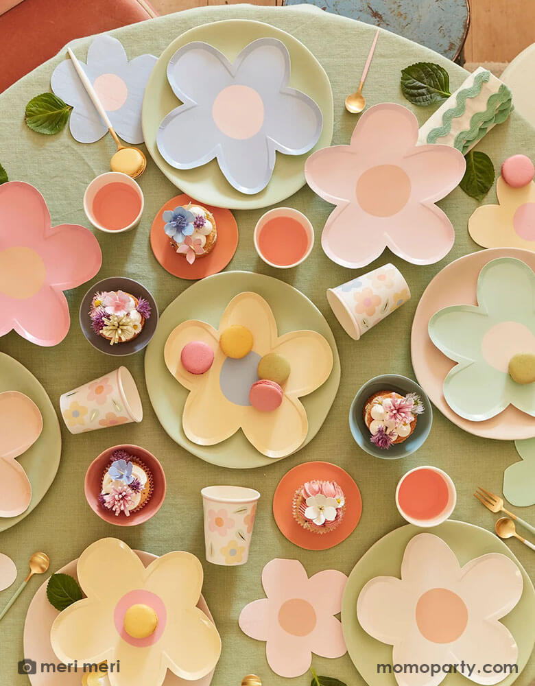 A round party table with adorable spring inspired treats and desserts featuring Momo Party's daisy shaped plates and napkins in multiple pastel colors, with pastel colored round plates underneath and happy flower party cups it makes a charming tablescape for a spring gathering, kid's daisy themed birthday or an Easter celebration.