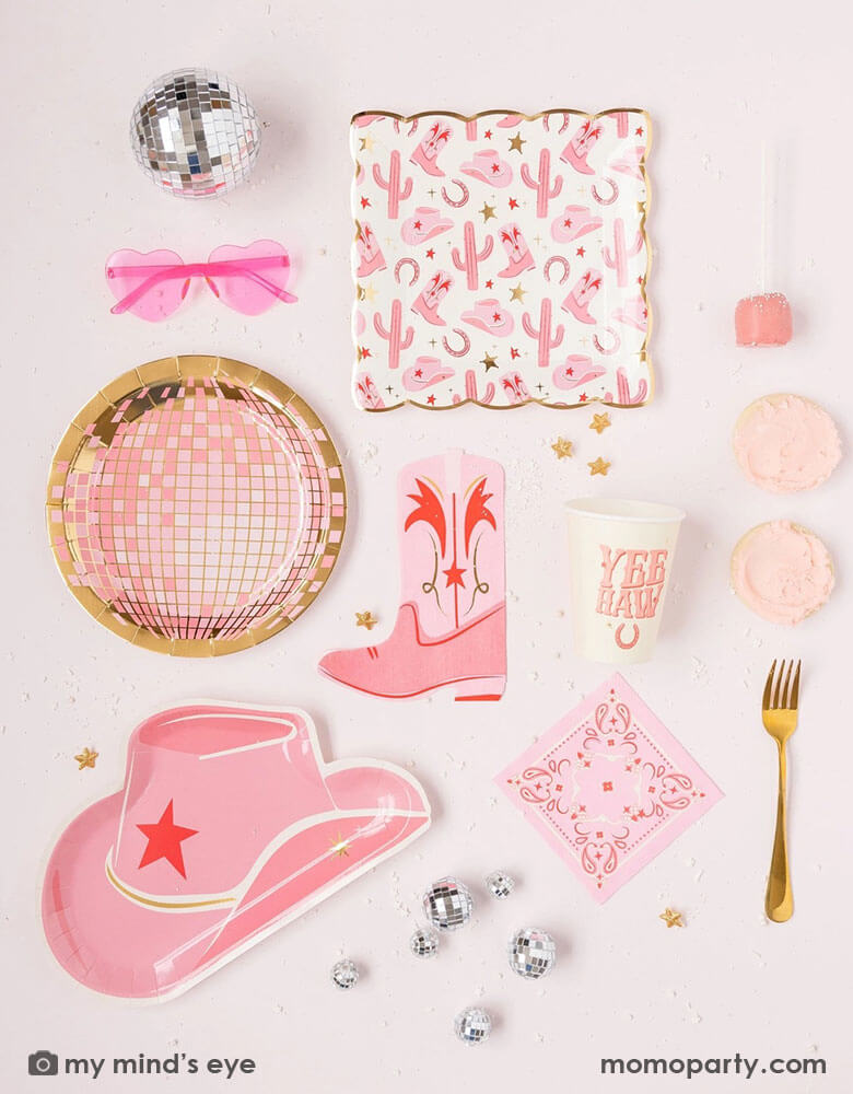A cowgirl rodeo Western themed party table features pink cowgirl themed party supplies from Momo Party including pink cowgirl boot shaped napkins, cowgirl hat shaped plates, pink disco ball shaped plates, pink bandana small napkins, yeehaw party cups and cowgirl pattern paper plates by My Mind's Eye, along with festive disco ball decorations, heart shaped sunglasses and pink treats, this makes a perfect inspo for kid's cowgirl themed birthday party or a disco cowgirl bachelorette party celebration!
