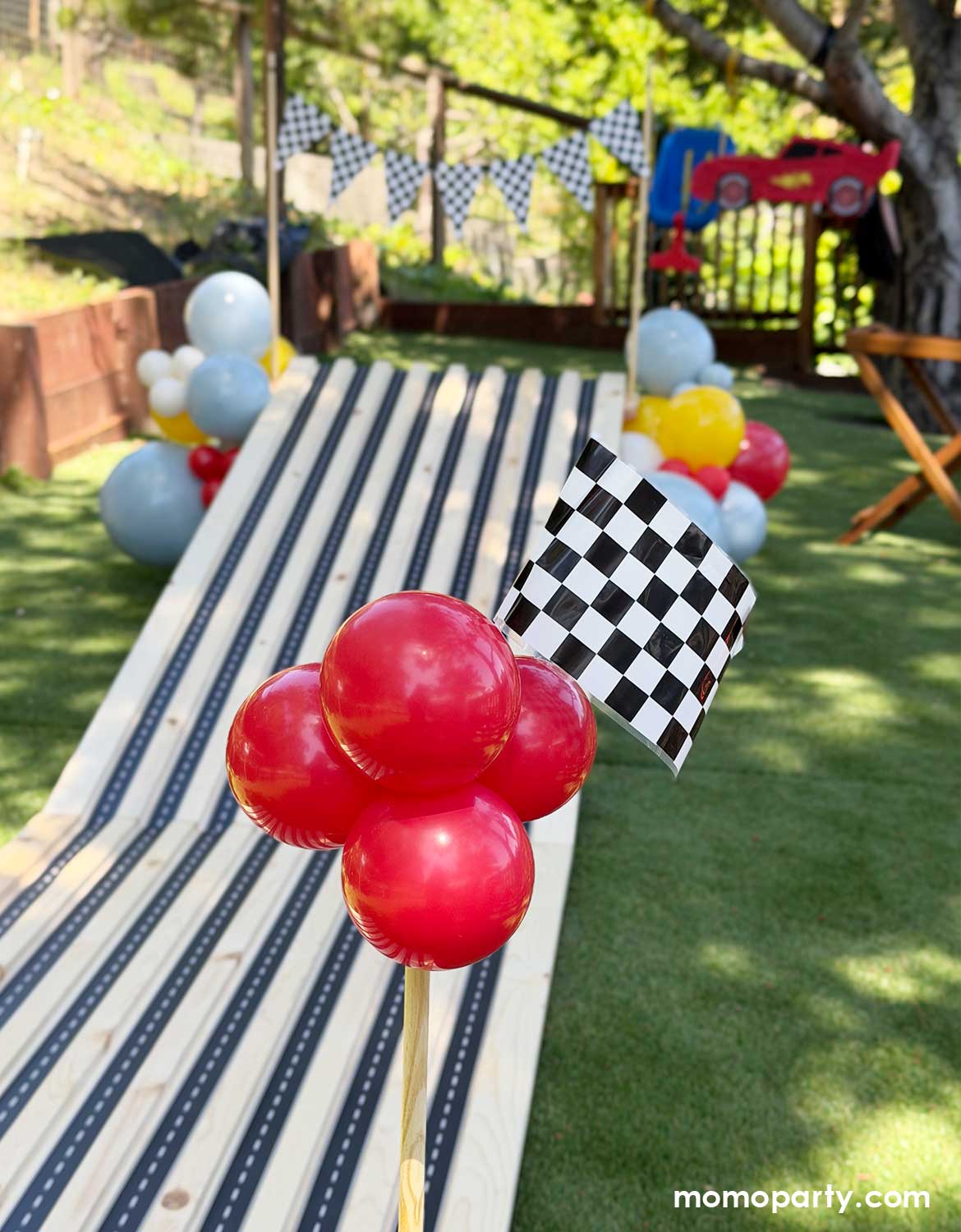 A kid's Disney Cars themed birthday party race track activity set up by Momo Party. This vroom vroom wooden race track for endless fun was decorated with festive balloons adorn with the race car checkered flags from Momo Party.  A perfect decoration inspo for boy's race car themed birthdays or Lightning Mcqueen themed parties.