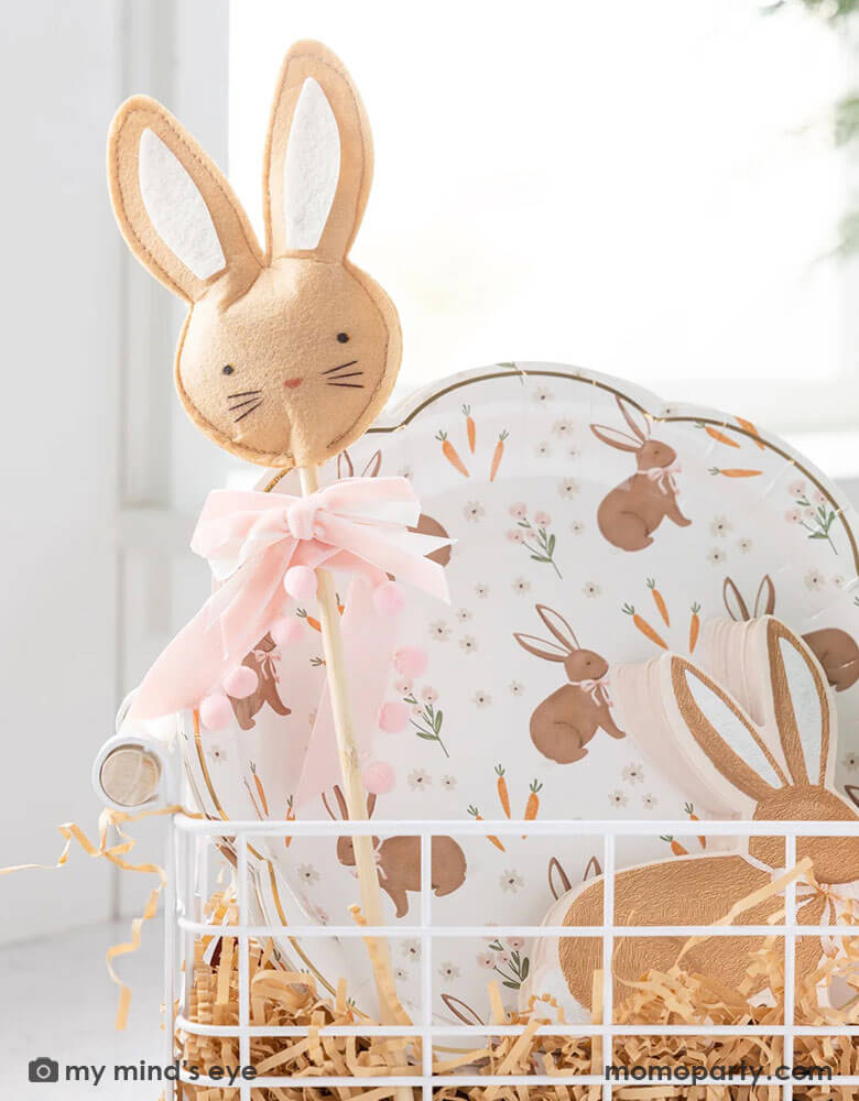A close up of an Easter occasion bin filled with Momo Party's Easter themed tableware, treat bags and kid's gift, including the 9" x 9" scatter rabbit plates, rabbit shaped napkins, Easter bunny wand and carrot shaped treat bags by My Mind's Eye.