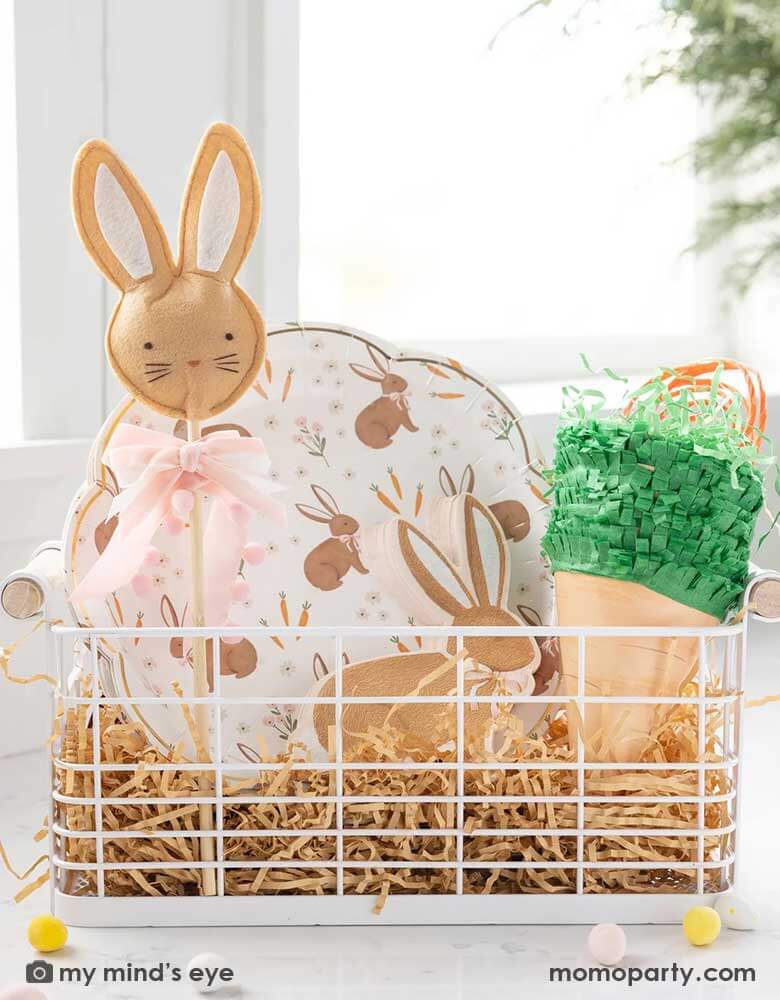 An Easter occasion bin filled with Momo Party's Easter themed tableware, treat bags and kid's gift, including the 9" x 9" scatter rabbit plates, rabbit shaped napkins, Easter bunny wand and carrot shaped treat bags by My Mind's Eye.