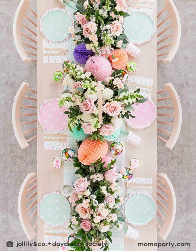 A beautiful Easter brunch table features Momo Party's Easter fun small plates along with striped party plates, cups, and napkins. In the middle of the table lays a blue gingham table runner which has baskets of spring flower arrangement and egg shaped honeycomb decorations in pastel colors, making this an adorable inspo for a Easter party tablesetting.
