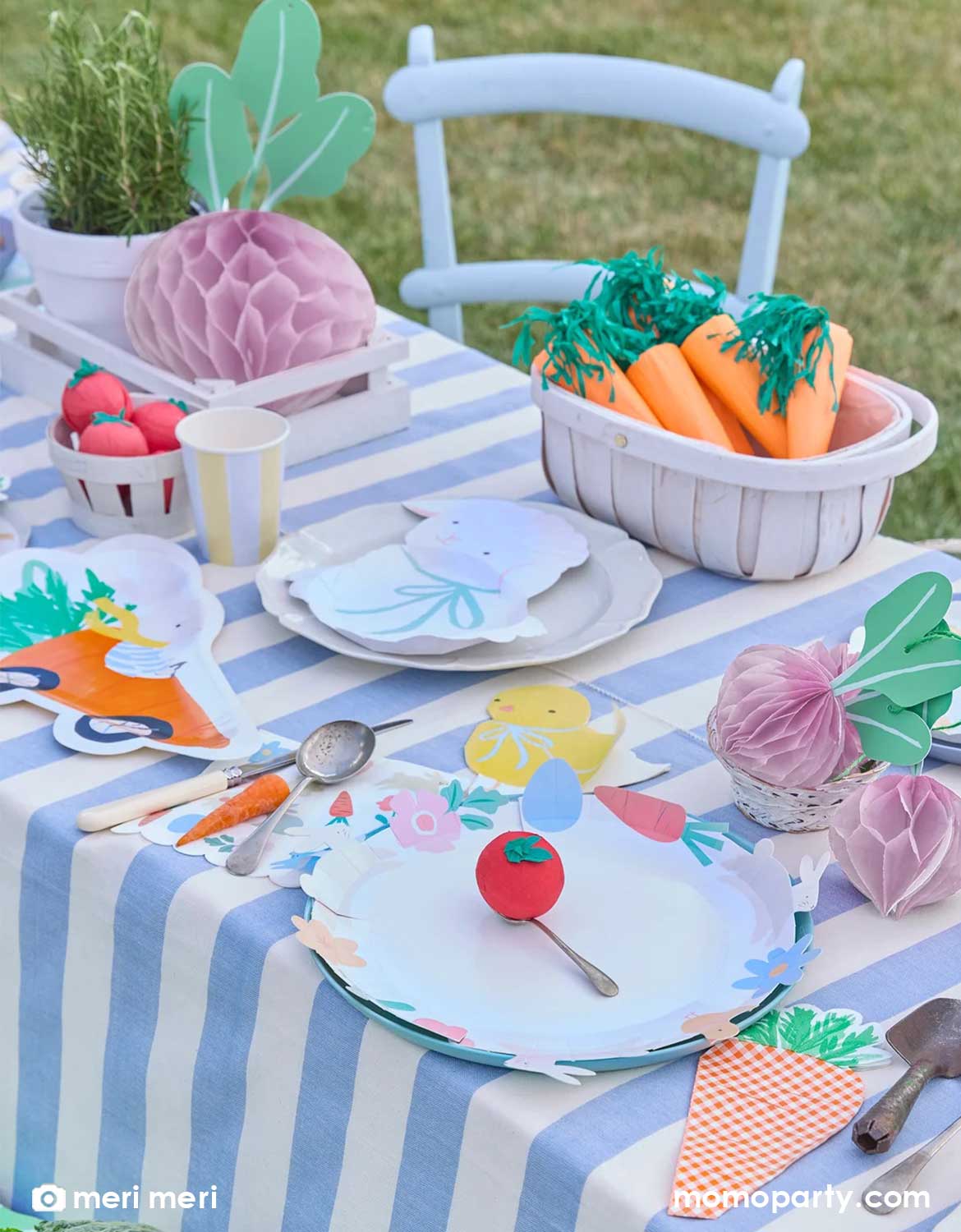 A children's spring-inspired party table setting featuring vegetable-themed decor, bunny and lamb shaped party plates and napkins on a blue striped tablecloth - a perfect set up for a festive spring or Easter celebration.
