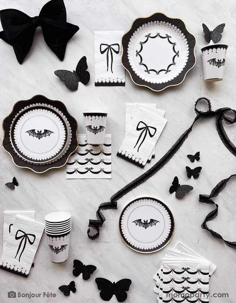 A chic Halloween party tablescape featuring elegant black and white Halloween party supplies with black bow accents from Momo Party, including party plates, cups, napkins and wall decorations. Perfect for a sophisticated Halloween bash for adults in this spooktacular season.