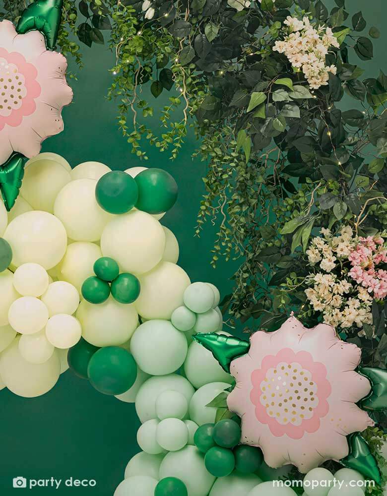 A spring inspired balloon garland in pastel yellow and mint colors peppered with some small emerald green as the green foliage adorned with two of Momo Party's 23" x 19" pink flower foil balloons. This balloon garland is next to a live leaf floral garland, makes this a great decoration for a garden party or spring inspired celebration.