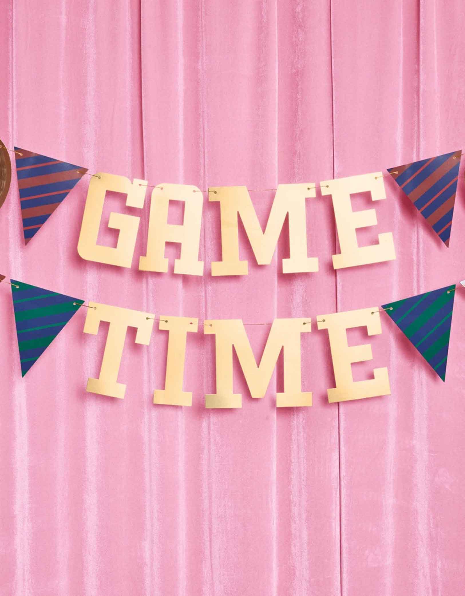 Momo Party's 4.5' football gold foil game time banner hung against a pink curtain.
