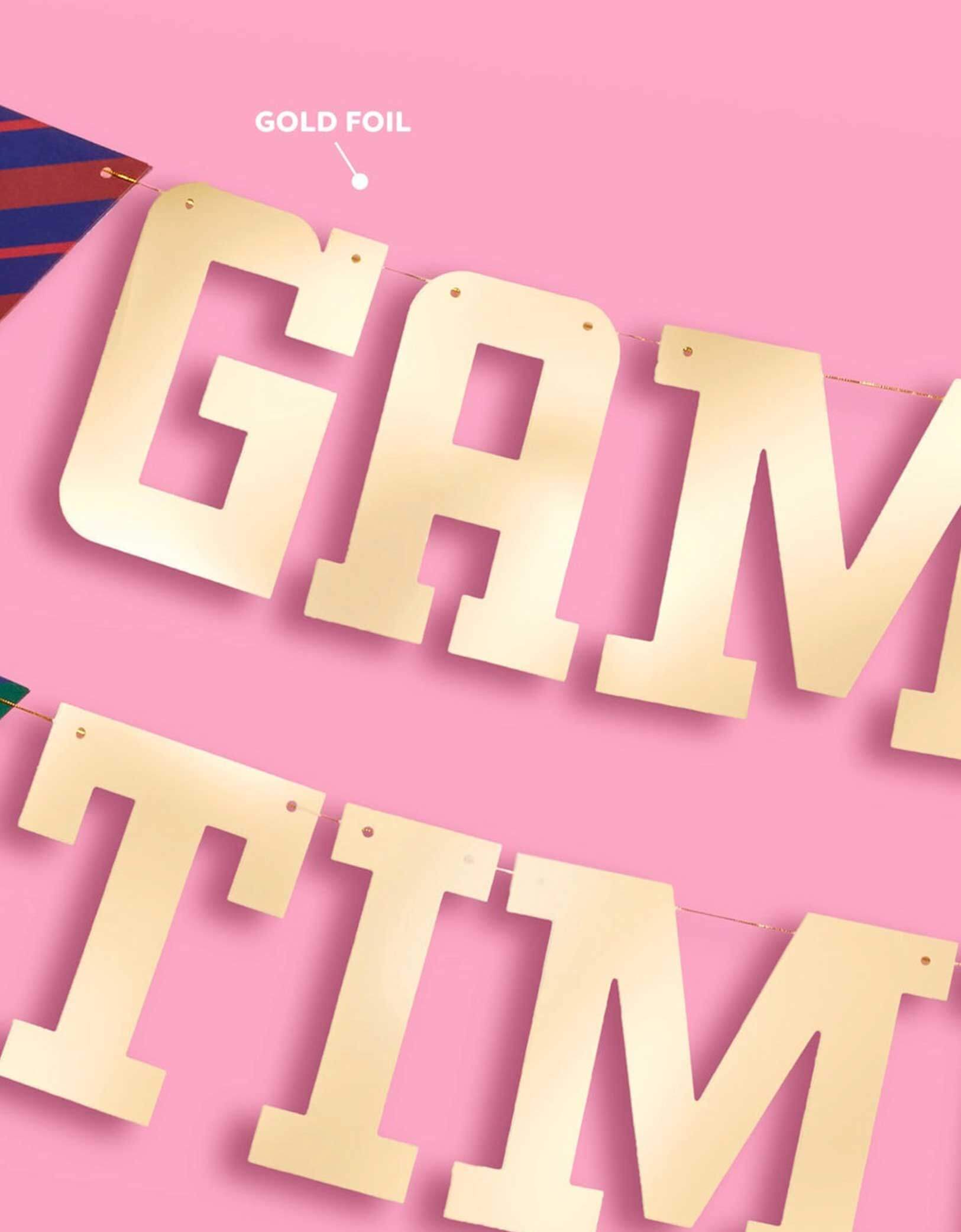 A close up shot of Momo Party's 4.5' football gold foil game time banner on a pink background.