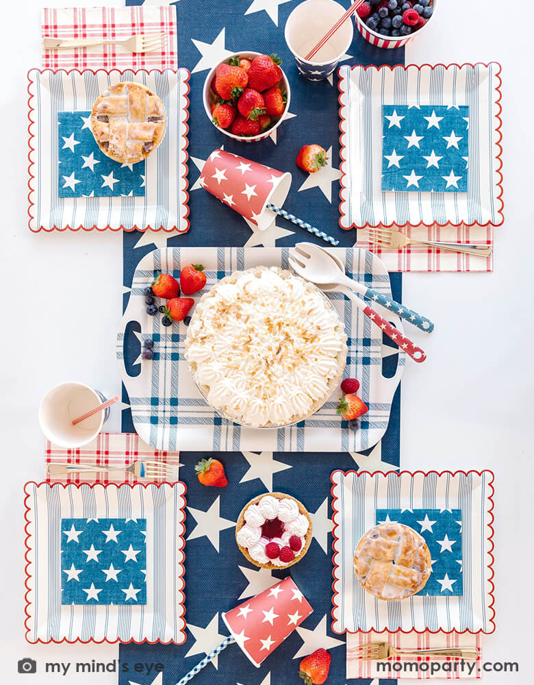 A patriotic themed table set featuring Momo Party's 9" navy and red scalloped stripe plates, 5" Hamptons navy star small napkins, 9 oz blue and red star party cups by My Mind's Eye. In the middle a pie is served on a reusable bamboo tray with elegant navy plaid pattern. With raspberry pies and mixed berries served on the navy star pattern runner, all makes a festive and perfect inspiration for Memorial Day BBQ party or 4th of July Independence Day celebration.