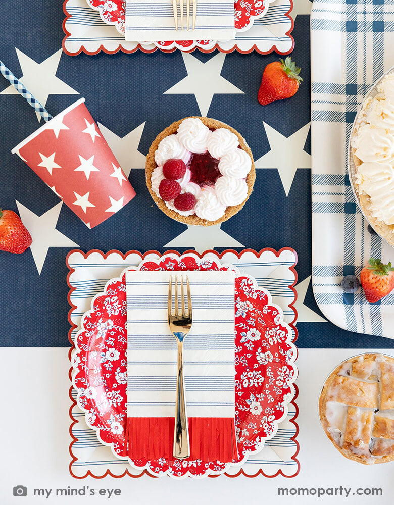 A festive patriotic theme tablescape featuring Momo Party's 9" navy and red scalloped stripe plates, red scalloped fringe guest napkins, 9 oz blue and red star party cups by My Mind's Eye. With raspberry pies and mixed berries served on the navy star pattern runner, all makes a festive and perfect inspiration for Memorial Day BBQ party or 4th of July Independence Day celebration.